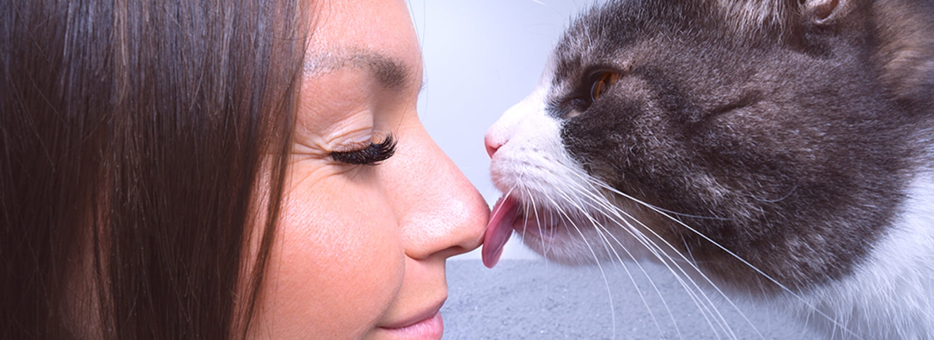 Un gros plan d'une femme les yeux fermés souriant pendant qu'un chat lui lèche le nez.